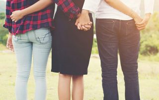 3 Menschen stehen mit Rücken zur Kamera Hand in Hand